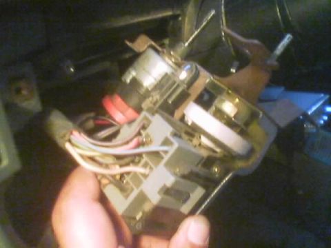1990 Ford Bronco - hand holds a removed switch assembly with red, white and striped wires and a round dial, near the underside of a vehicle dashboard.