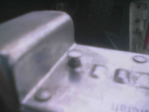 1990 Ford Bronco - dark, out-of-focus close-up of a worn metal panel with a protruding stud, bolt holes and faint embossed lettering.