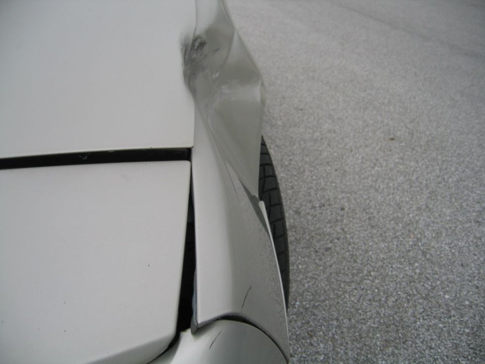 White car fender with significant damage and a visible tire