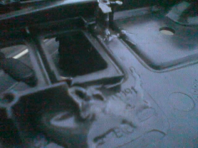 Dim view of a black-painted floor pan area with an opening and embossed markings