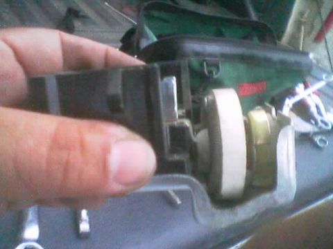1990 Ford Bronco - hand holds a black plastic switch housing exposing a white gear and brass mechanism, with tools and a green bag in the background.