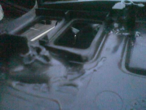 1990 Ford Bronco - dim, dark photo of a black-painted vehicle floor pan showing rectangular openings, body seams and a shifter or lever boot area.