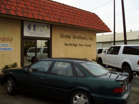 1993 Ford Taurus - A dark green sedan is parked in front of Orme Brothers, Inc. Northridge Auto Supply, with other vehicles visible in the background.