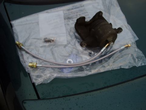 1993 Ford Taurus - Brake caliper and braided brake lines are laid out on plastic packaging, likely for an upgrade or repair.