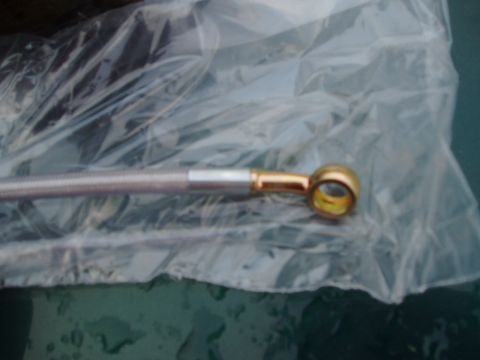 1993 Ford Taurus - A close-up view of a braided brake hose fitting, likely for a vehicle's braking system.