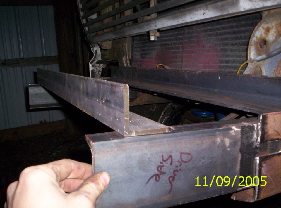 Metal frame pieces attached to a vehicle's front end, with a radiator visible behind. A hand is holding a piece of metal