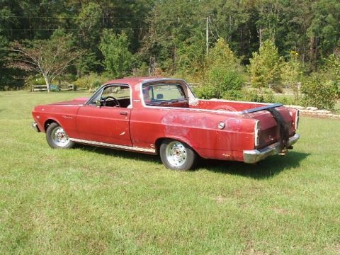 1966 Ford Ranchero - A faded red 1960s Ford Ranchero car-based pickup shown from a rear three-quarter angle, sitting on a grassy lawn with trees in the backgrou…