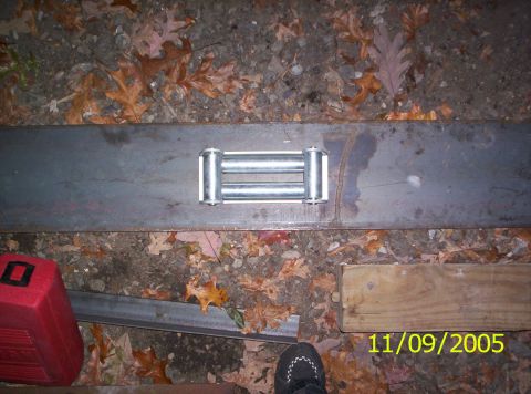 1985 Ford Bronco - A winch roller fairlead is mounted on a metal plate, surrounded by fallen leaves and debris.