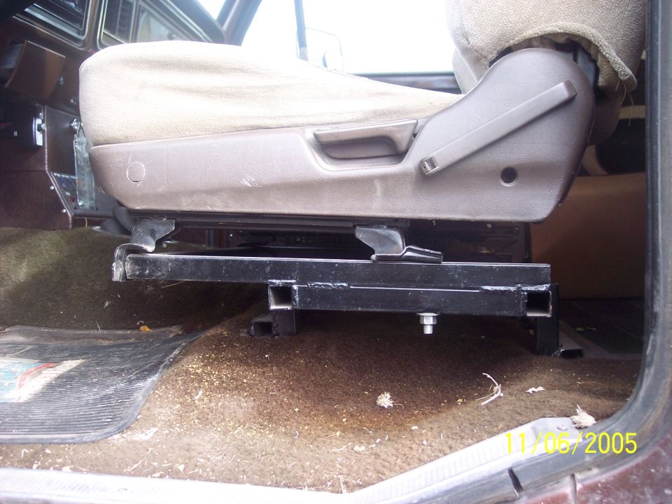 Tan bucket seat mounted on custom black square-tube riser bracket inside a truck cab