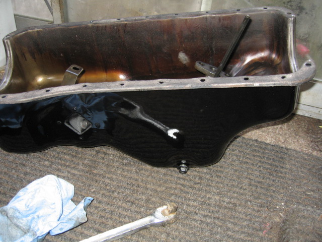 Removed engine oil pan painted black sitting on carpet with a wrench and rag