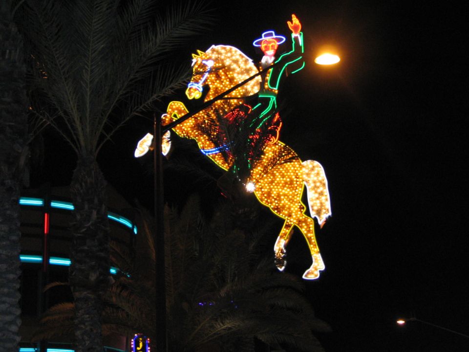 Neon cowboy riding a horse decoration at night with palm trees and building lights
