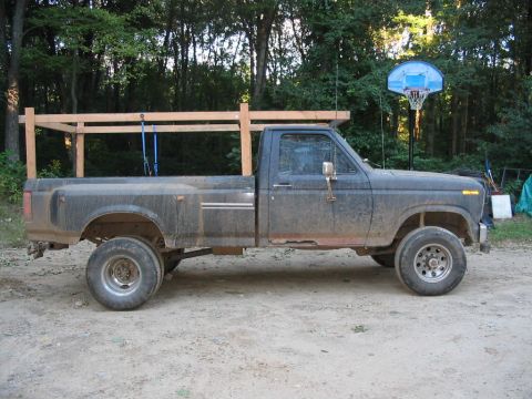 1985 Ford F-350 - A weathered Ford pickup truck, equipped with a custom wooden rack, is parked outdoors on a dirt surface.