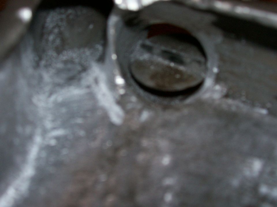 Blurry macro of a metal casting with round opening and slotted plug, white residue on surface