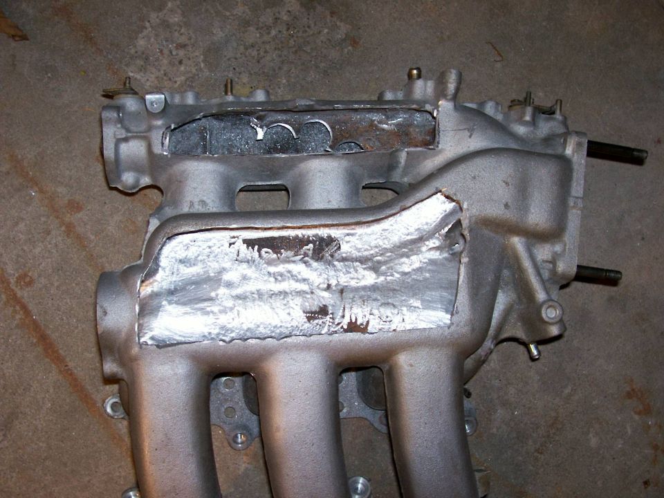 Aluminum intake manifold on concrete floor with cut-open plenum and rough weld repair patch