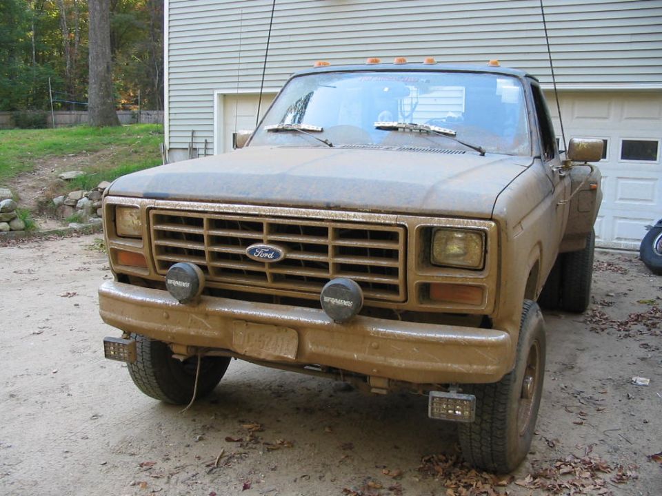 Square-body Ford 4x4 dually covered in dried tan mud by a garage