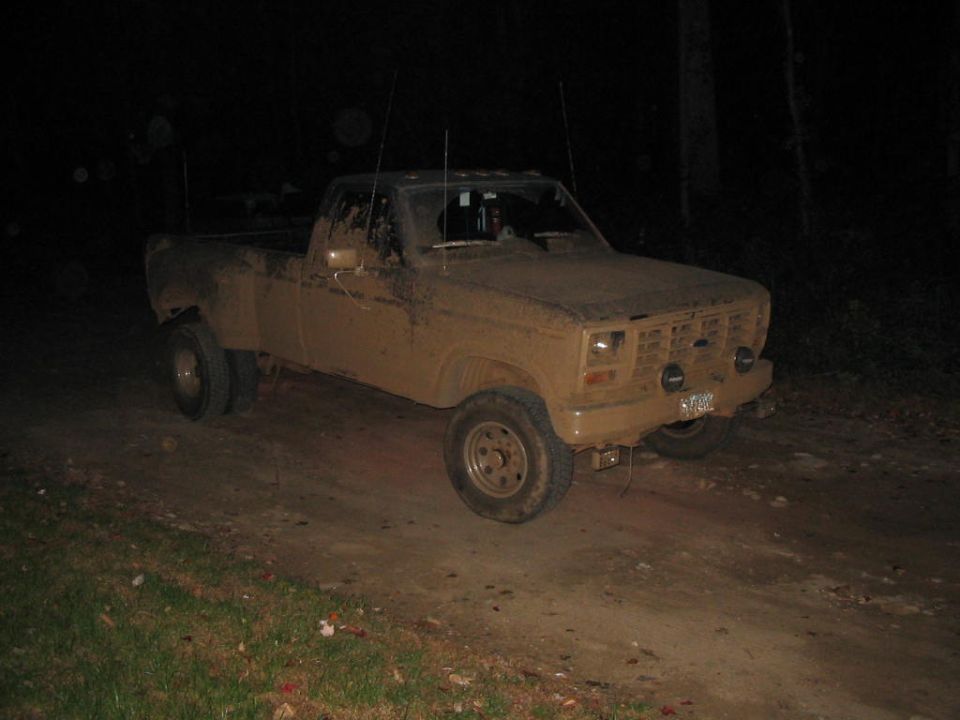 Mud-covered square-body Ford 4x4 pickup on a dirt road at night