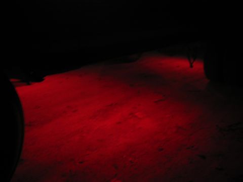 1985 Ford F-350 - Red underglow lights illuminate the ground at night, casting a dark shadow from a vehicle.