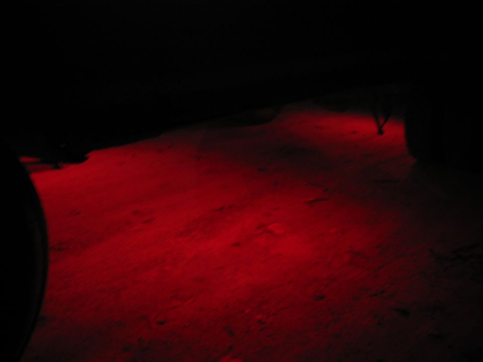 Ground illuminated by red underglow lights at night, with a dark silhouette of a vehicle on the right