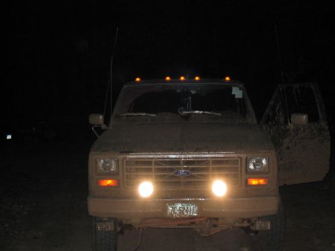 1985 Ford F-350 - A muddy Ford F-Series truck is seen at night with its headlights illuminated and the driver's door ajar.