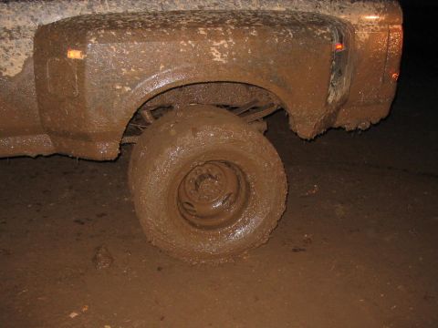 1985 Ford F-350 - A truck's rear wheel and fender are heavily caked in mud, obscuring details of the vehicle.
