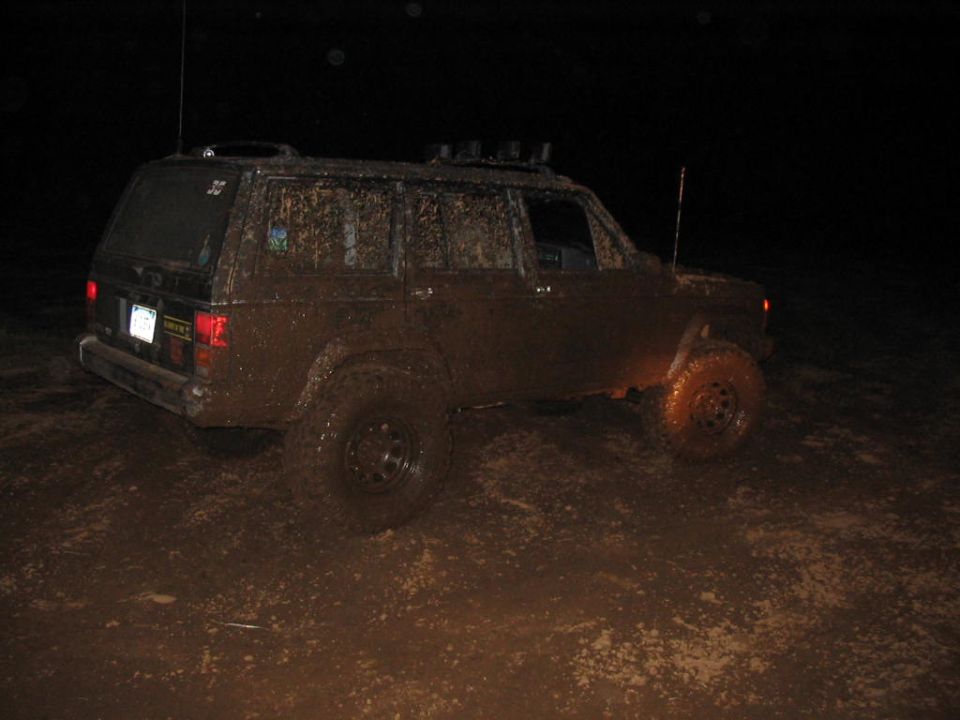 Mud-covered SUV with roof rack, seen at night