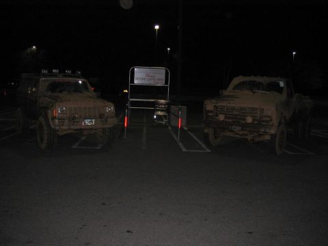 1985 Ford F-350 - Two mud-covered trucks are parked in a lot at night, illuminated by streetlights.