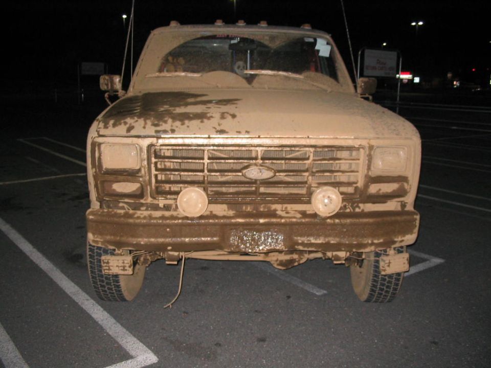 Mud-covered 1980s Ford truck front view. Grille and headlights are caked in mud