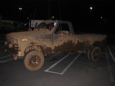 1985 Ford F-350 - A heavily mud-splattered pickup truck sits in a parking lot at night, its body caked in dirt.