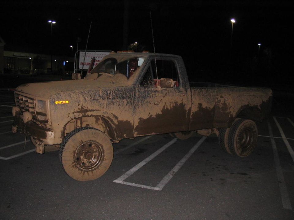 Mud-covered pickup truck, 3/4 front view, showing dual rear wheels and a dirty grille