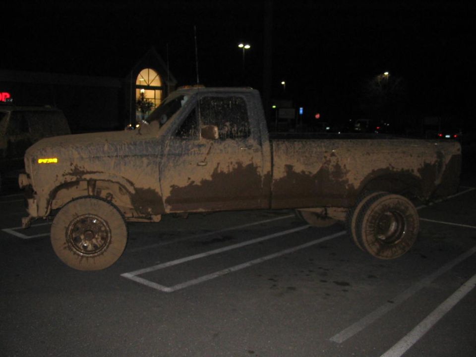 Lifted mud-covered 4x4 regular cab long bed pickup parked at night in a store lot