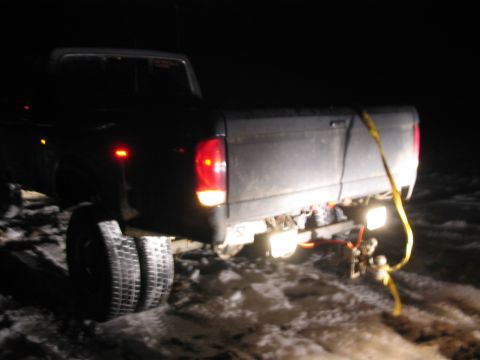 1985 Ford F-350 - Dually pickup truck's rear end is visible at night, with a yellow strap connected to its hitch.