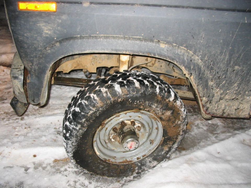 Truck wheel with aggressive tread in snow, dark fender above, orange turn signal