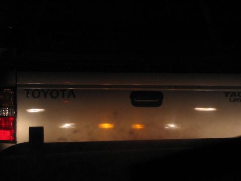 1985 Ford F-350 - The rear of a Toyota pickup truck is shown at night, with the tailgate illuminated.