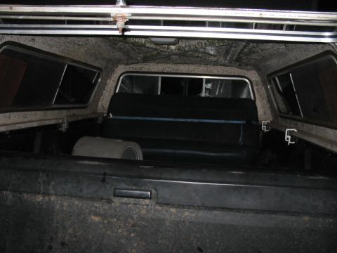 1985 Ford F-350 - Interior view of a truck bed with a camper shell, revealing a bench seat and a spare tire.