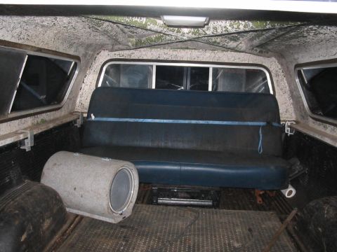 1985 Ford F-350 - The interior of a pickup truck bed shows a bench seat, a subwoofer, and a camper shell.
