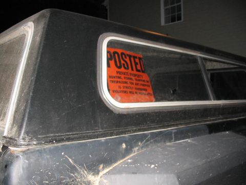 1985 Ford F-350 - Orange posted sign on the window of a black truck cap reads 'Private Property Hunting, Fishing, Trapping on Trespassing for Any Purpose is…