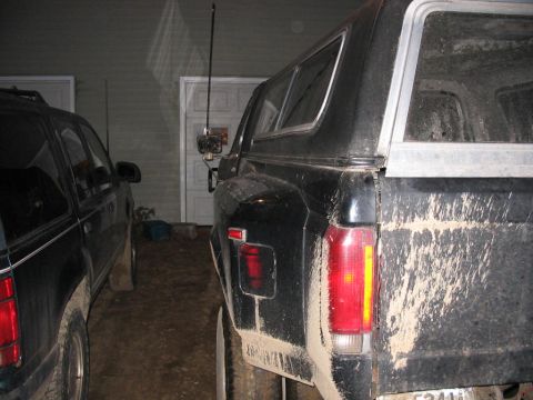 1985 Ford F-350 - A muddy pickup truck with a camper shell is parked next to an SUV in front of a garage.