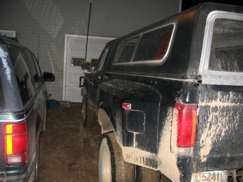 1985 Ford F-350 - A muddy black pickup truck with a camper shell is parked next to another vehicle.