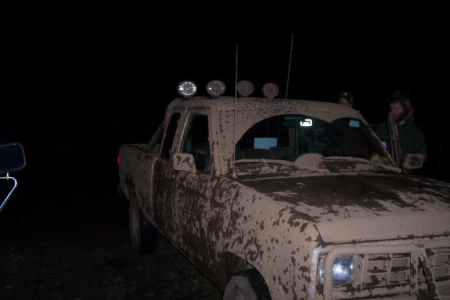Muddy pickup truck with light bar on roof, people in cab