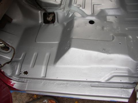 1995 Ford Bronco - The interior floor pan of a vehicle has been painted silver, showing some wiring and a drain hole.