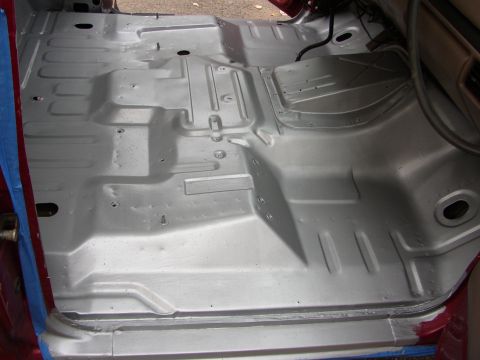 1995 Ford Bronco - The interior floor pan of a vehicle has been painted silver, revealing its underlying structure and mounting points.
