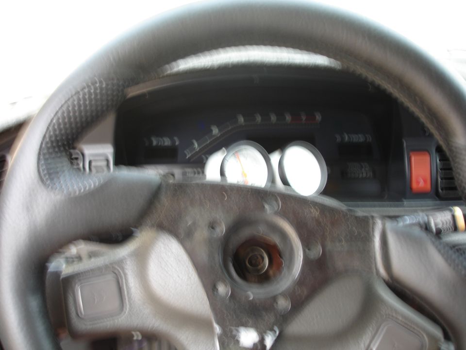 Car interior showing steering wheel, dashboard gauges, and a red button