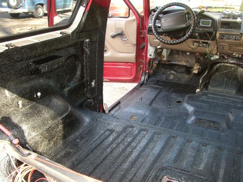 1995 Ford Bronco - The interior of a red Ford Bronco shows extensive application of black spray-on bedliner to the floor and lower door panels.
