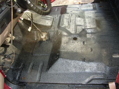 1995 Ford Bronco - The interior floor of a vehicle has been coated with a black, textured material, with some wiring visible.