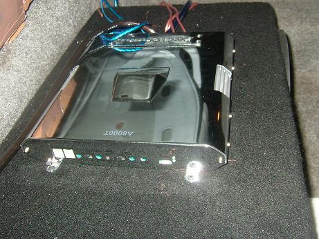1992 Ford Crown Victoria - A car amplifier is shown mounted on a carpeted surface, with visible wiring.