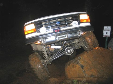 1995 Ford Bronco - A modified white Ford Bronco navigates rocky terrain at night, with its front tires elevated.