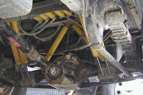 1984 Ford Bronco - Undercarriage view showing yellow shock absorbers and leaf springs, with visible "SUPERMOTORS" text at the bottom.