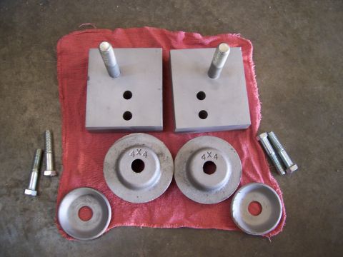 1983 Ford Bronco - Two TTB spring adapter blocks and four washers, two stamped 4x4, are laid out on a red cloth.