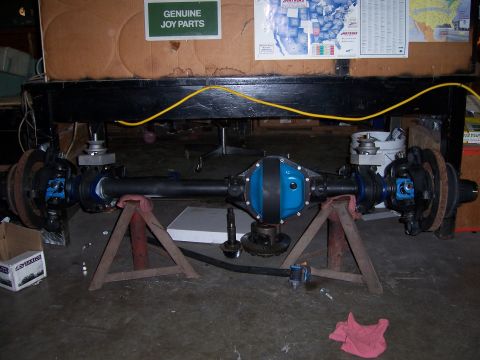 1983 Ford Bronco - A front axle assembly is displayed on jack stands, with a "Genuine Joy Parts" sign in the background.