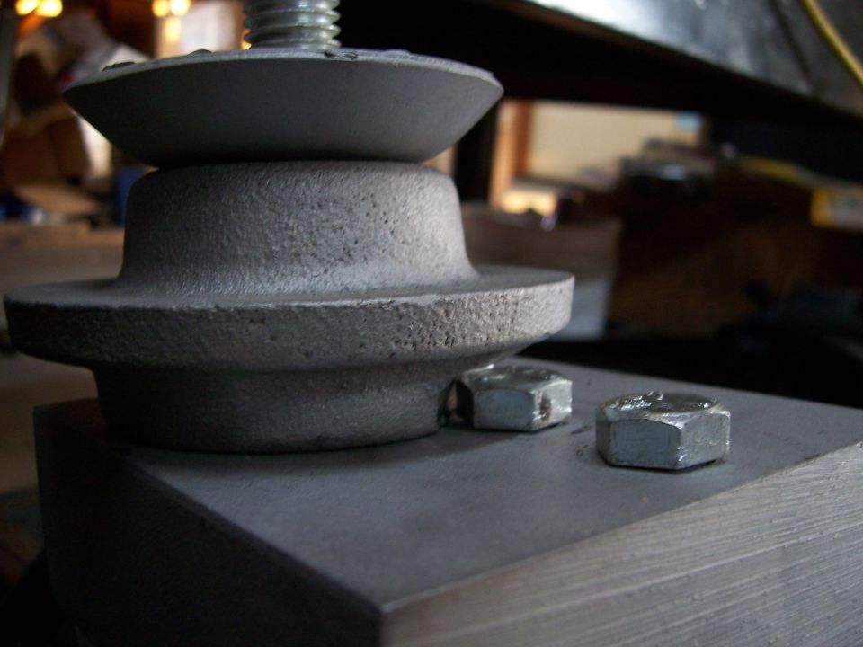 Gray metal suspension component with a threaded bolt and two hex nuts on a flat surface